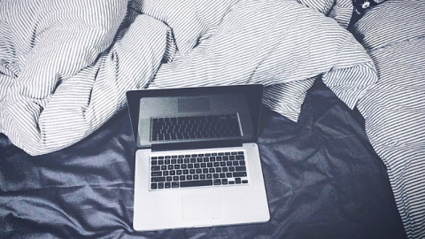 A laptop next to a messy duvet