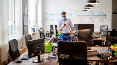 A lone man in a mask in an empty office looking at a phone