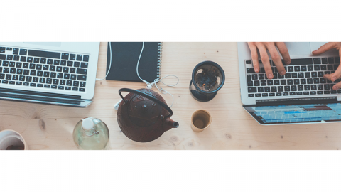 A workspace with laptops, teapots and miscellaneous curated cups and notebooks